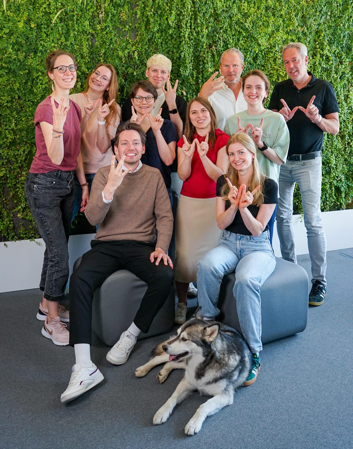 Worksdone-Team und Office-Dog Ari vor einer begrünten Wand.